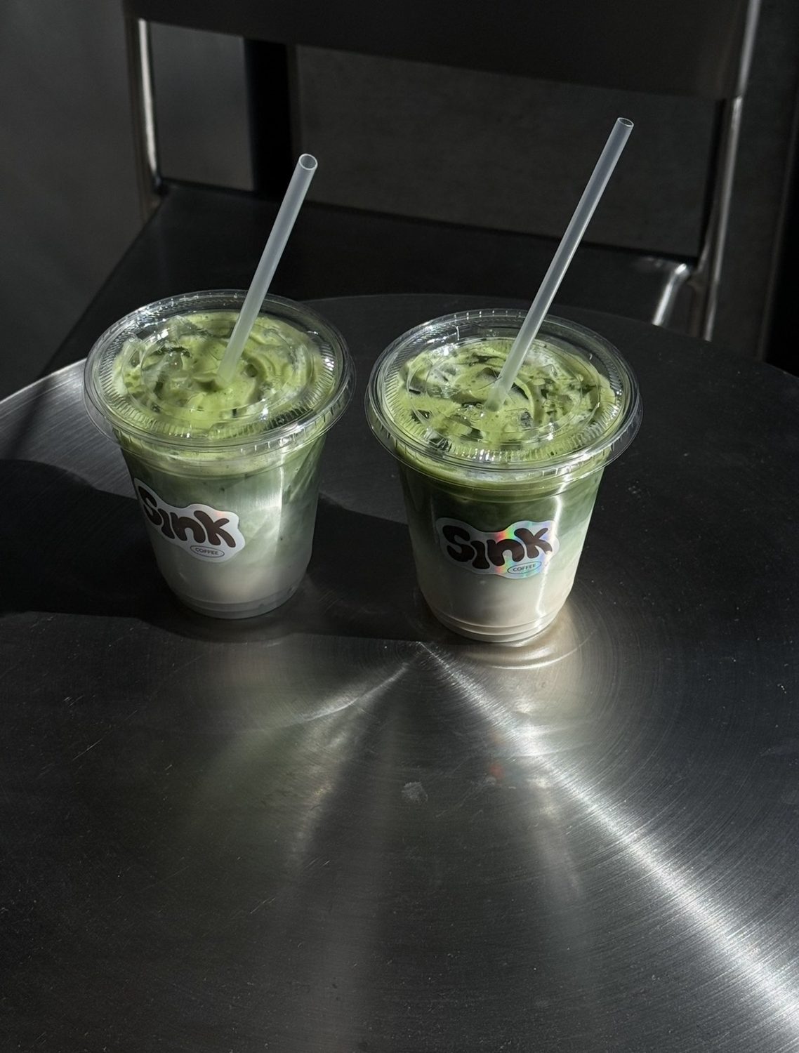 Two iced matcha lattes in Sink coffee cups on a steel table at Sink Reformer, Aarhus