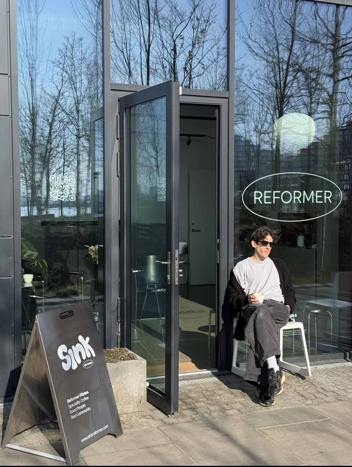 Guest with a coffee in the sun outside the entrance of Sink Reformer, Aarhus Ø
