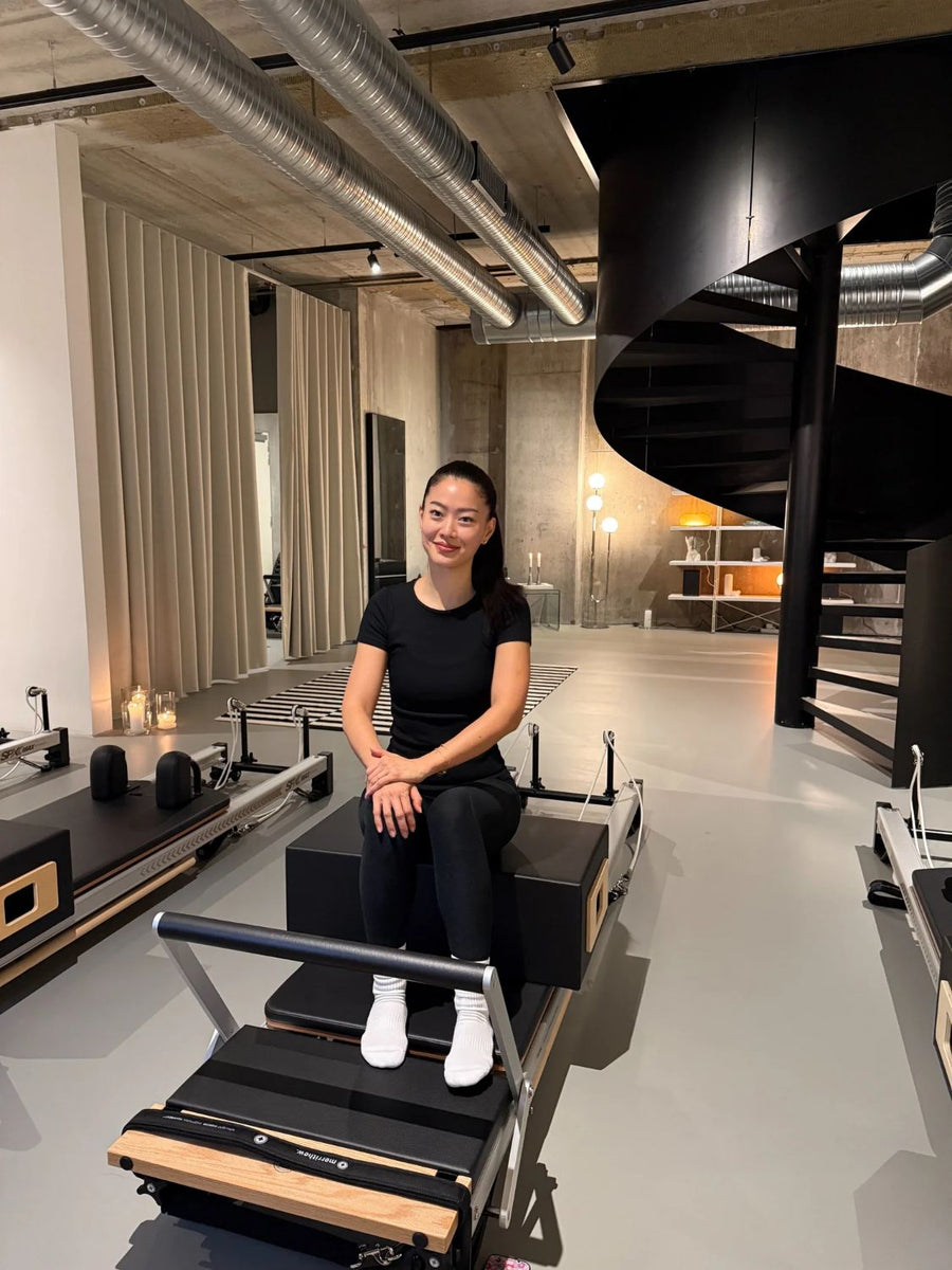 Jane, Pilates teacher, sitting on a reformer by the spiral staircase at Sink Reformer, Aarhus
