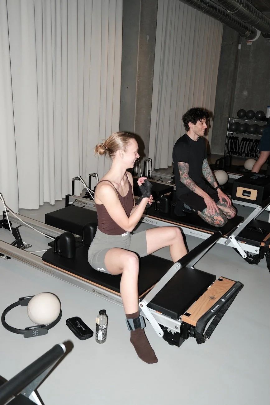 Two clients smiling on reformers during a Pilates class at Sink Reformer