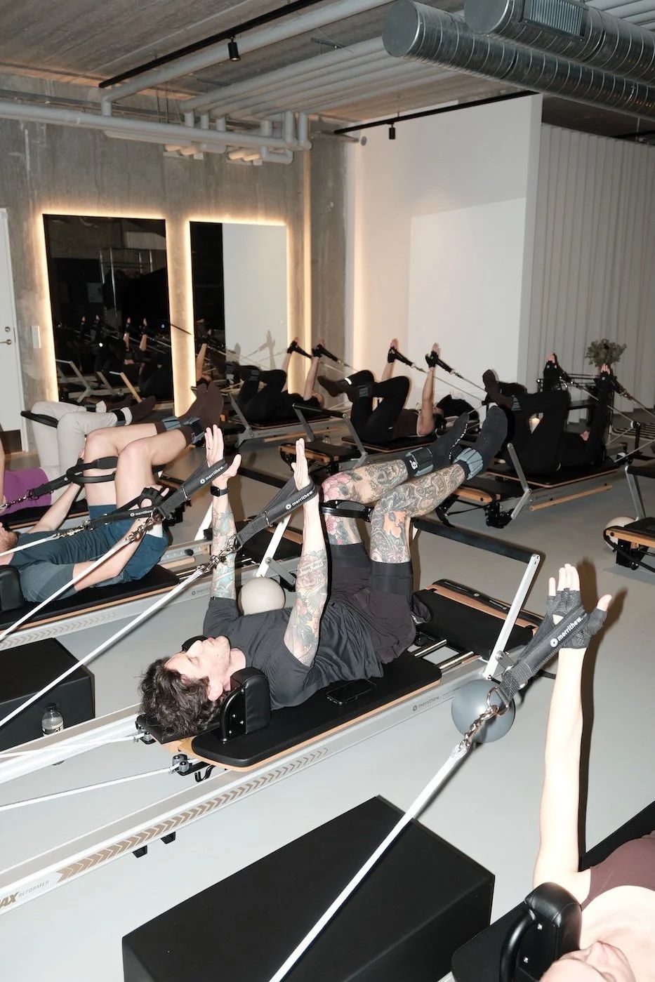Reformer Pilates class doing a reach and pull exercise with straps at Sink Reformer