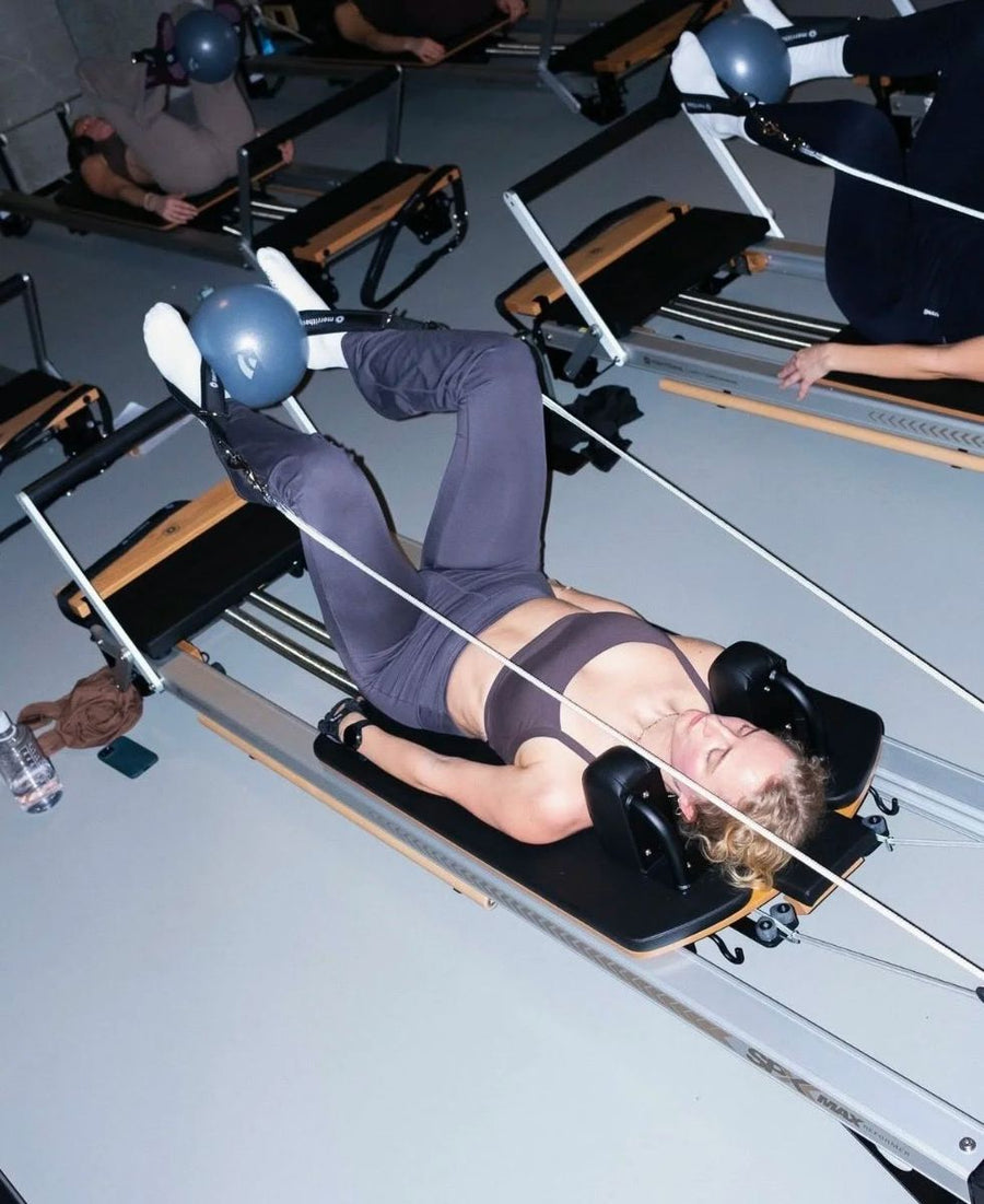 Client lying on a reformer with a ball between her feet during a class at Sink Reformer, Aarhus