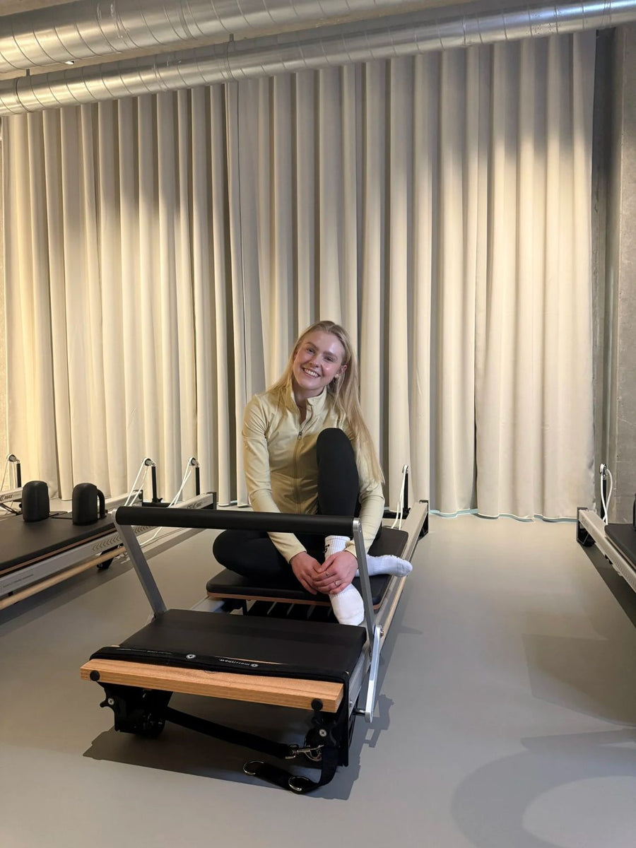 Aleks, reformer Pilates teacher, sitting on a reformer at Sink Reformer, Aarhus